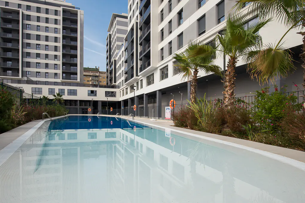 Outdoor pool with clear water reflecting modern apartment buildings and palm trees on a sunny day.