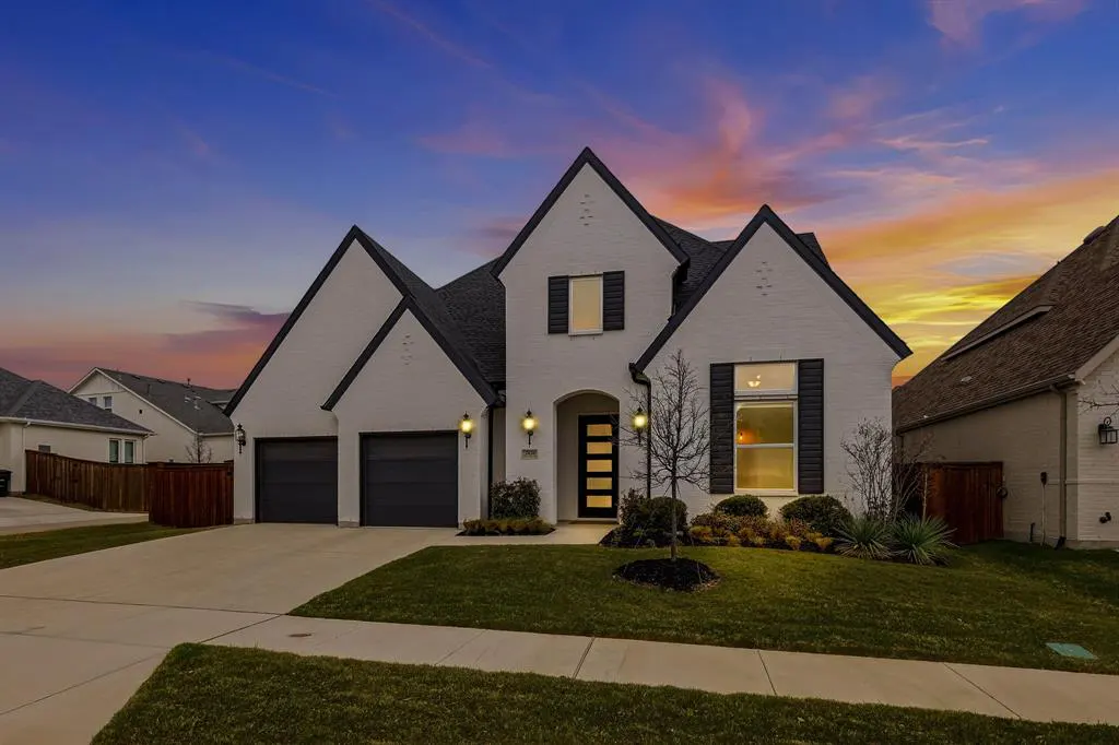 Two-story white brick house with black trim, black shutters, and a black garage door at dusk.