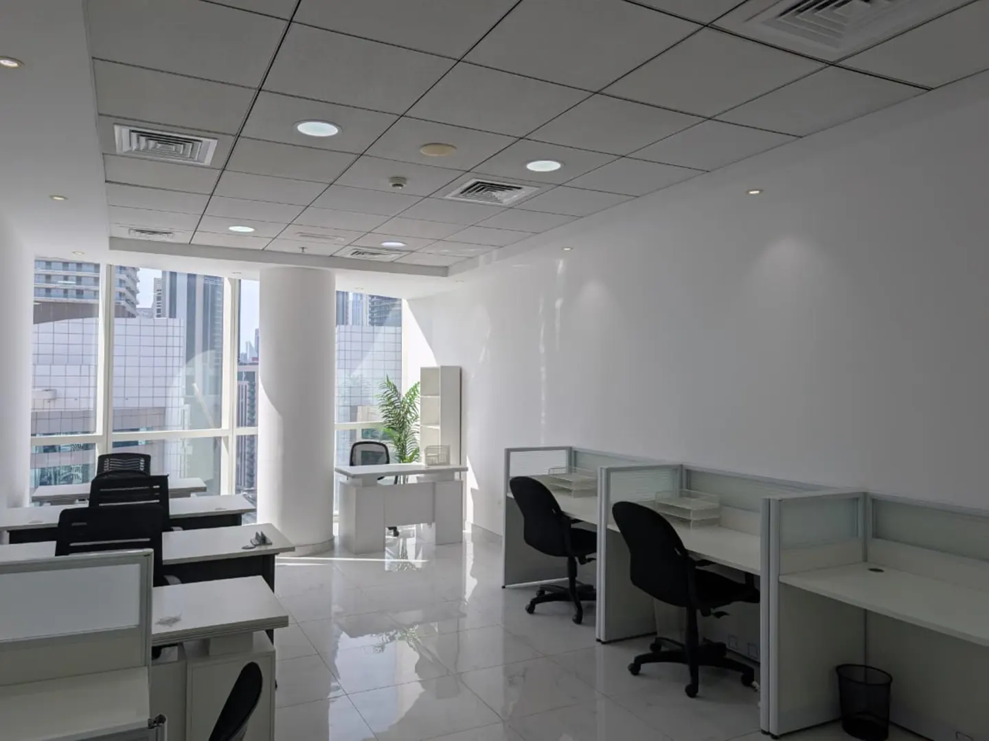 Bright, empty office space with white walls, tile floors, and cubicles. Large windows offer a city view.