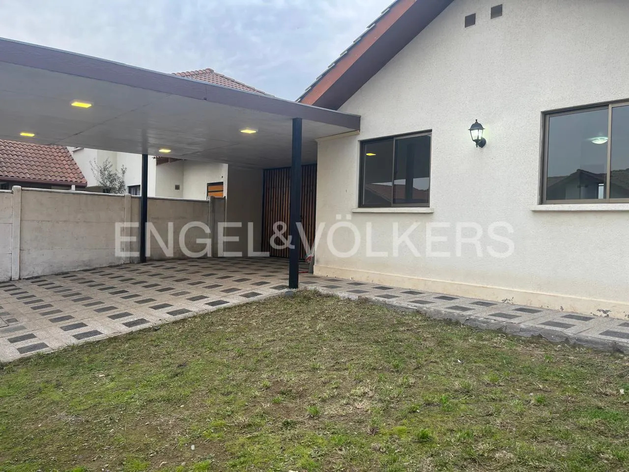 Exterior of a one-story house with a carport, lawn, and the Engel & Völkers logo.