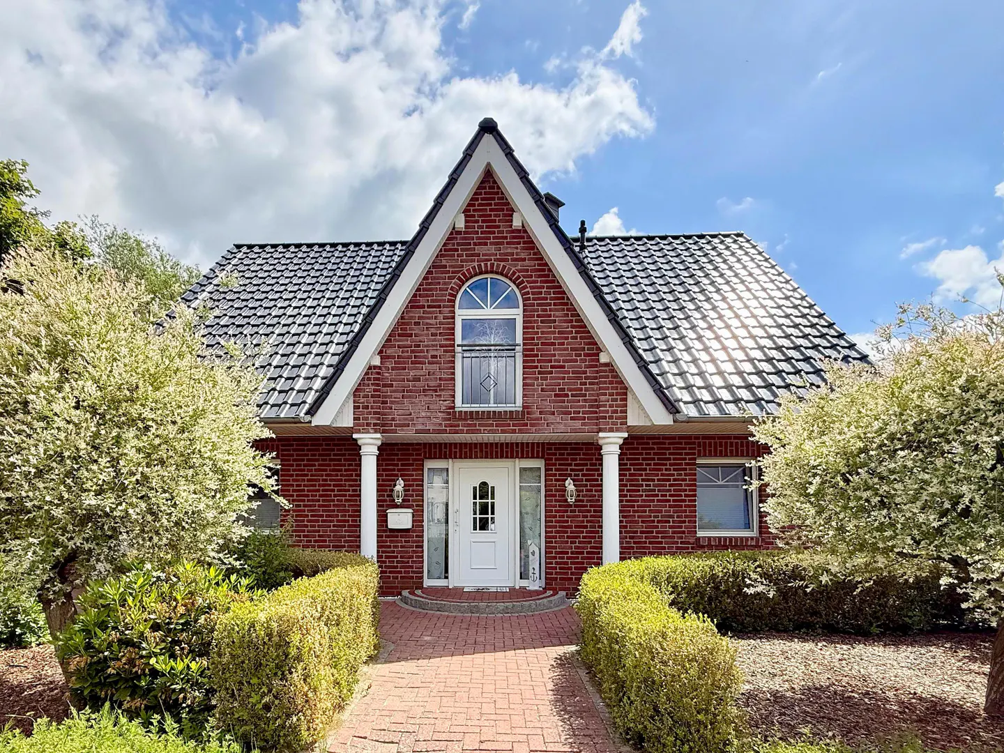 Red brick house with a black tiled roof, white trim, and a brick walkway leading to the front door.