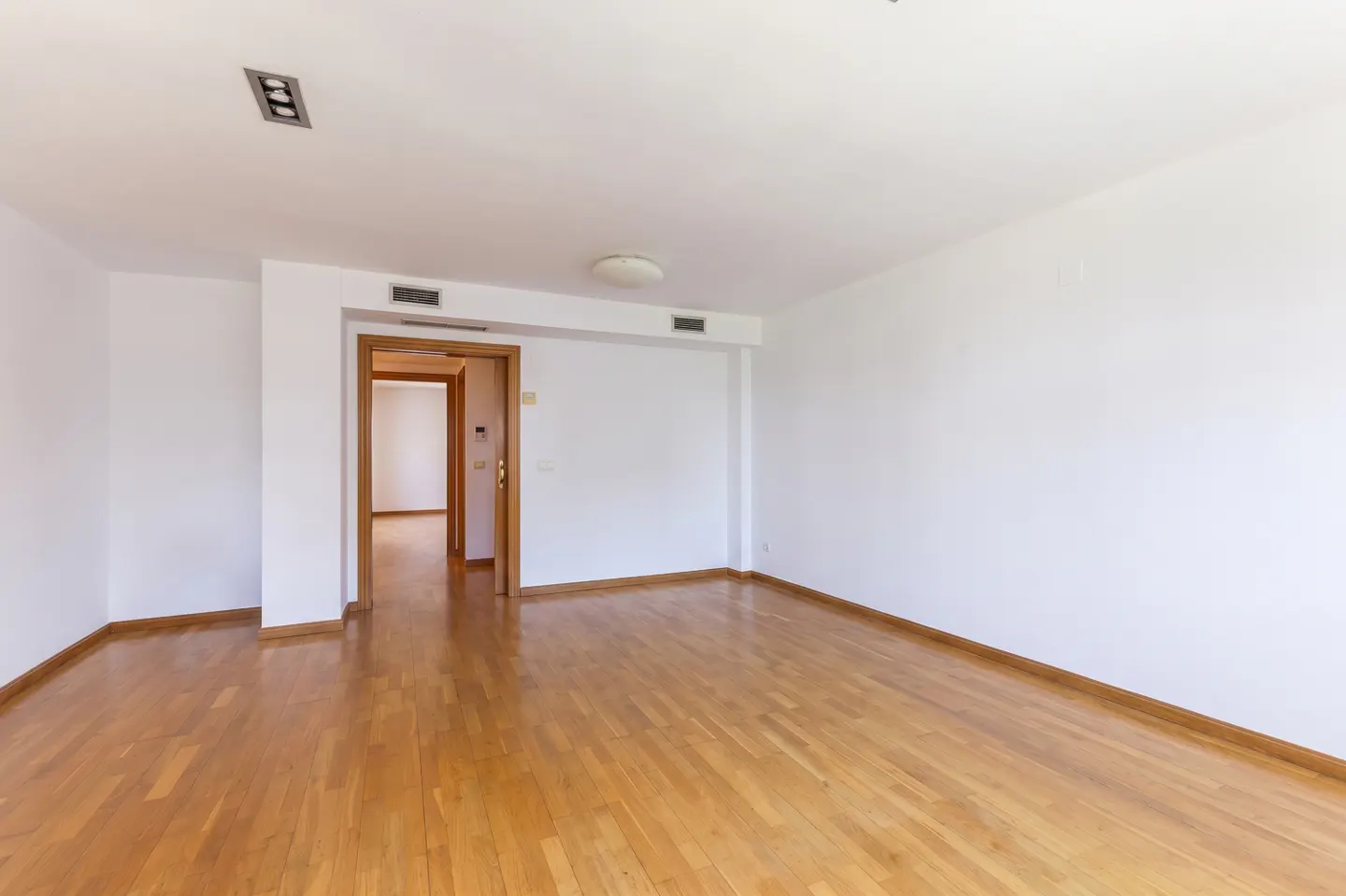 Bright, empty room with hardwood floors, white walls, and a doorway leading to another room.