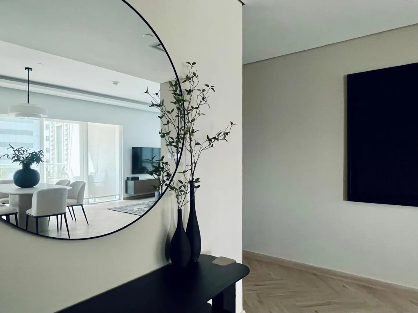 Interior view with a round mirror reflecting a dining area, black vases with branches, and a black console table.