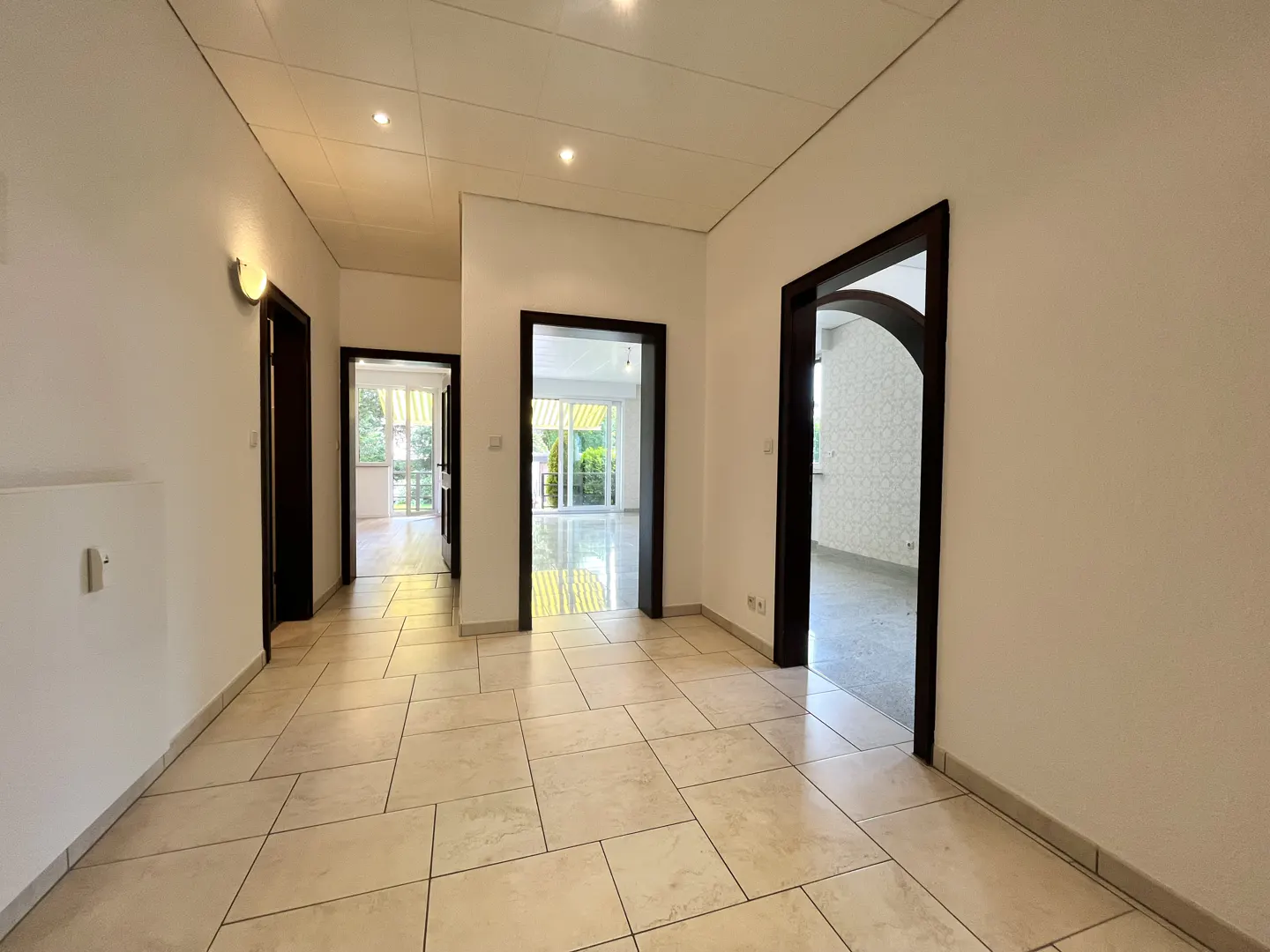 Bright hallway with light-colored tile flooring, white walls, and three dark-framed doorways leading to other rooms.