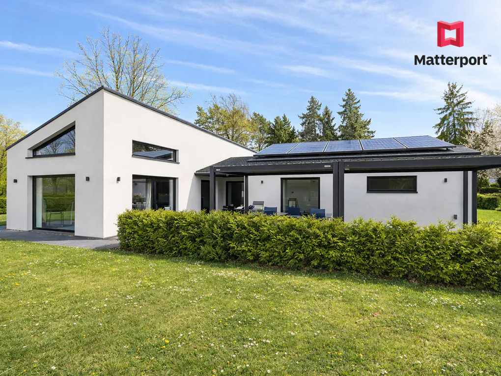 Exterior view of a modern white house with black trim, solar panels, and a green lawn under a blue sky.