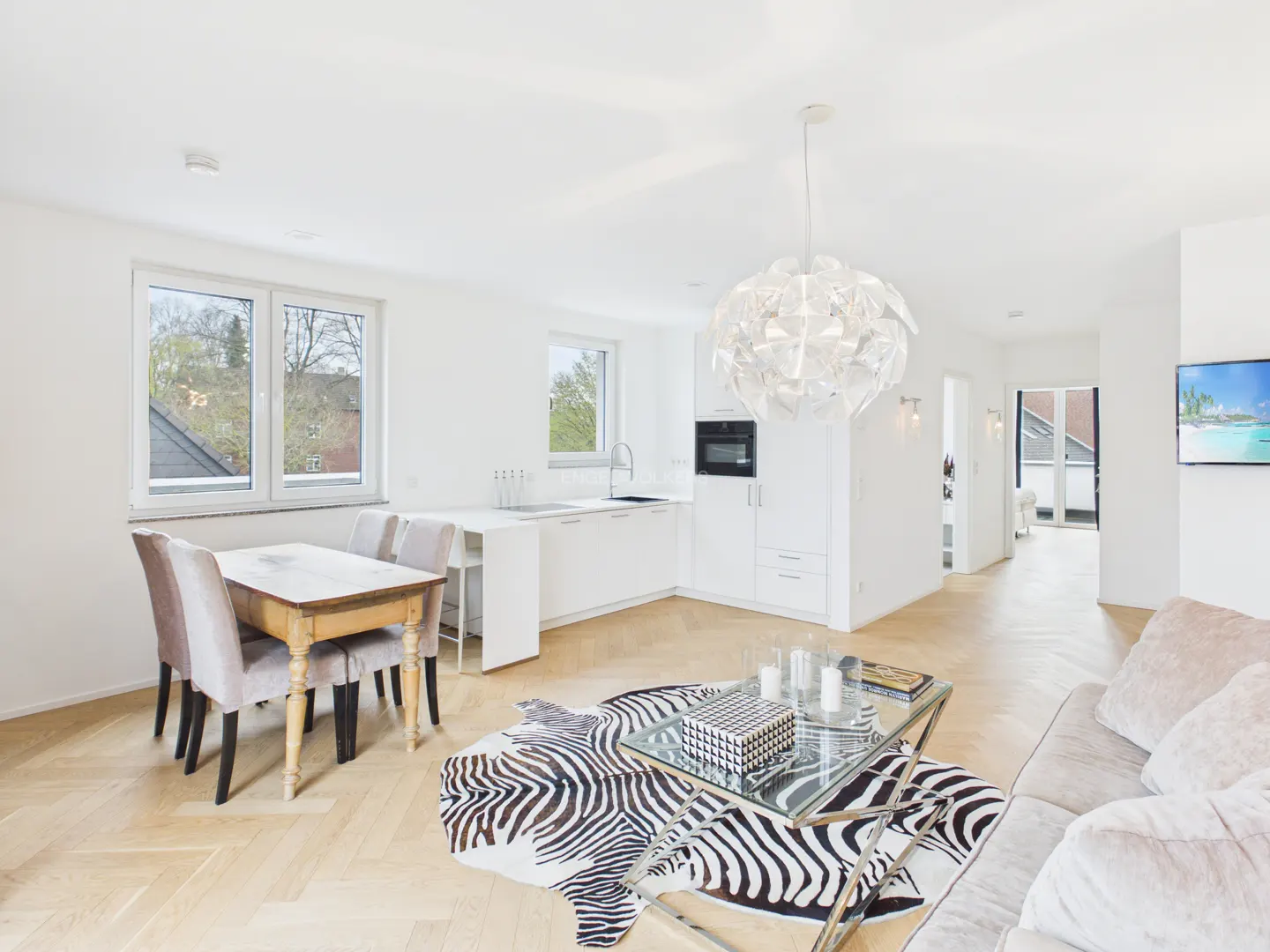 Bright, open-concept living space with white walls, wood floors, and a zebra-print rug. A dining table and kitchen are visible.