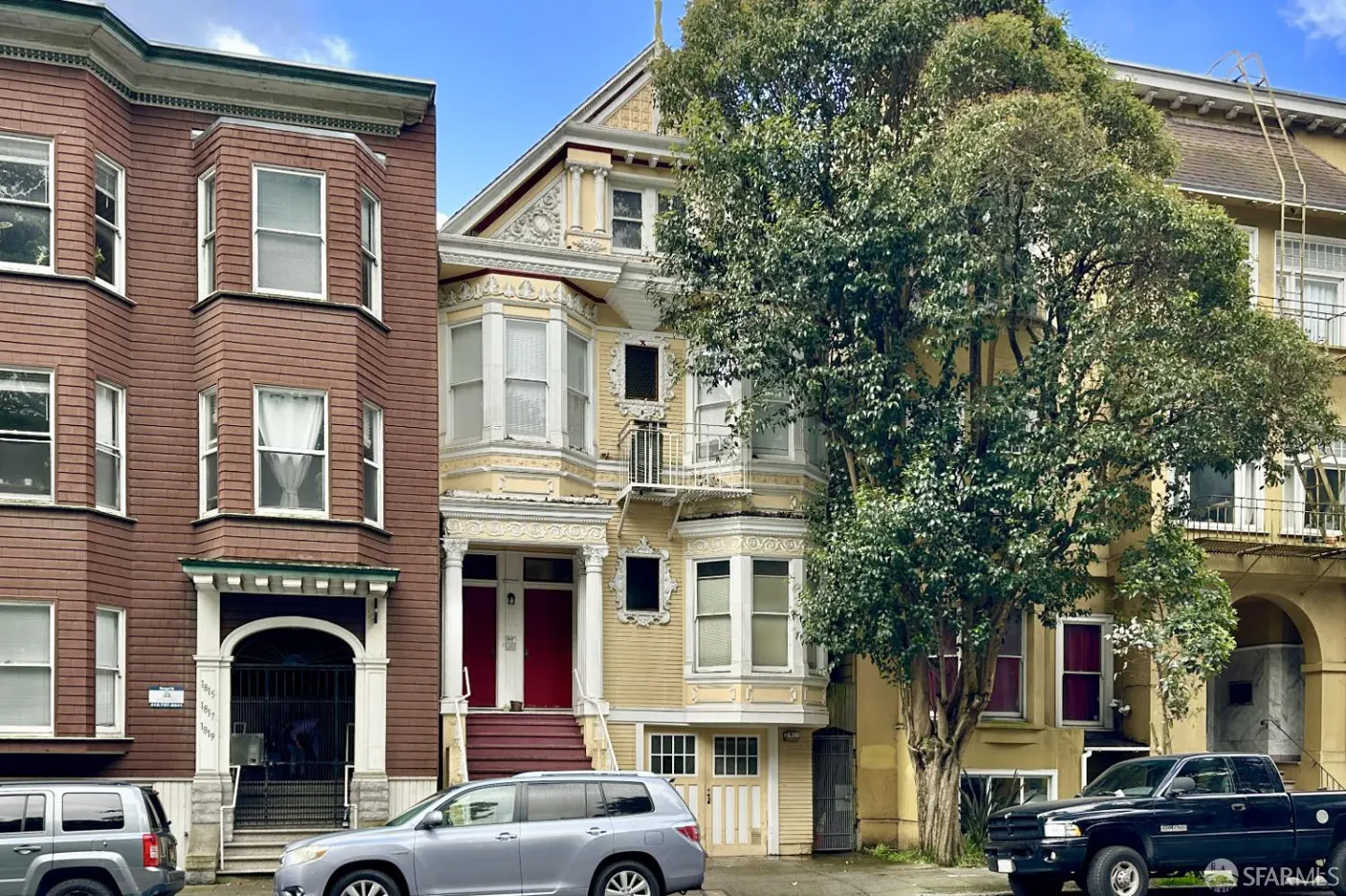 Street view of three Victorian-style houses in San Francisco, with cars parked in front. The center house is yellow with red doors.