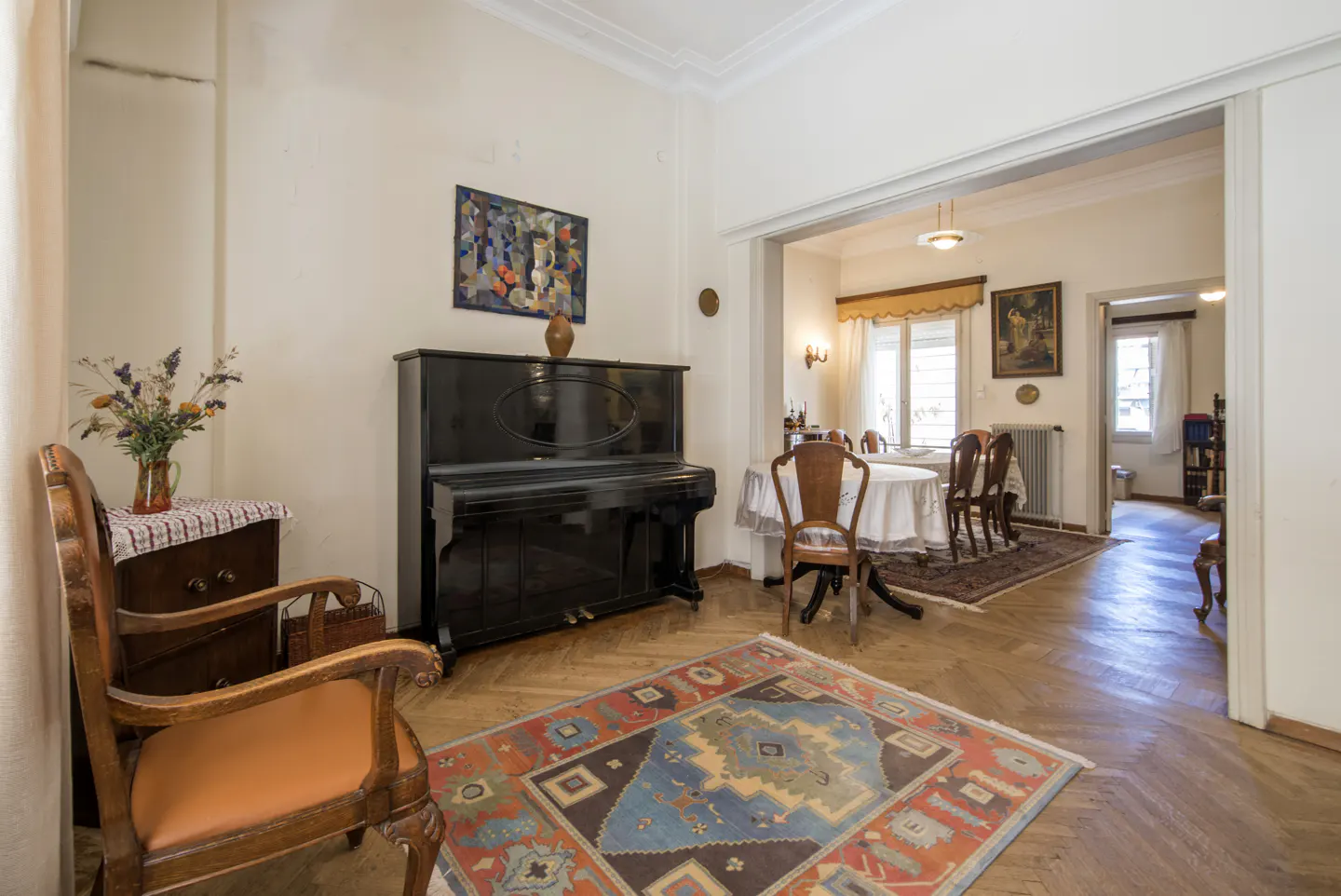 A living room with a black piano, a colorful rug, and a dining room in the background.