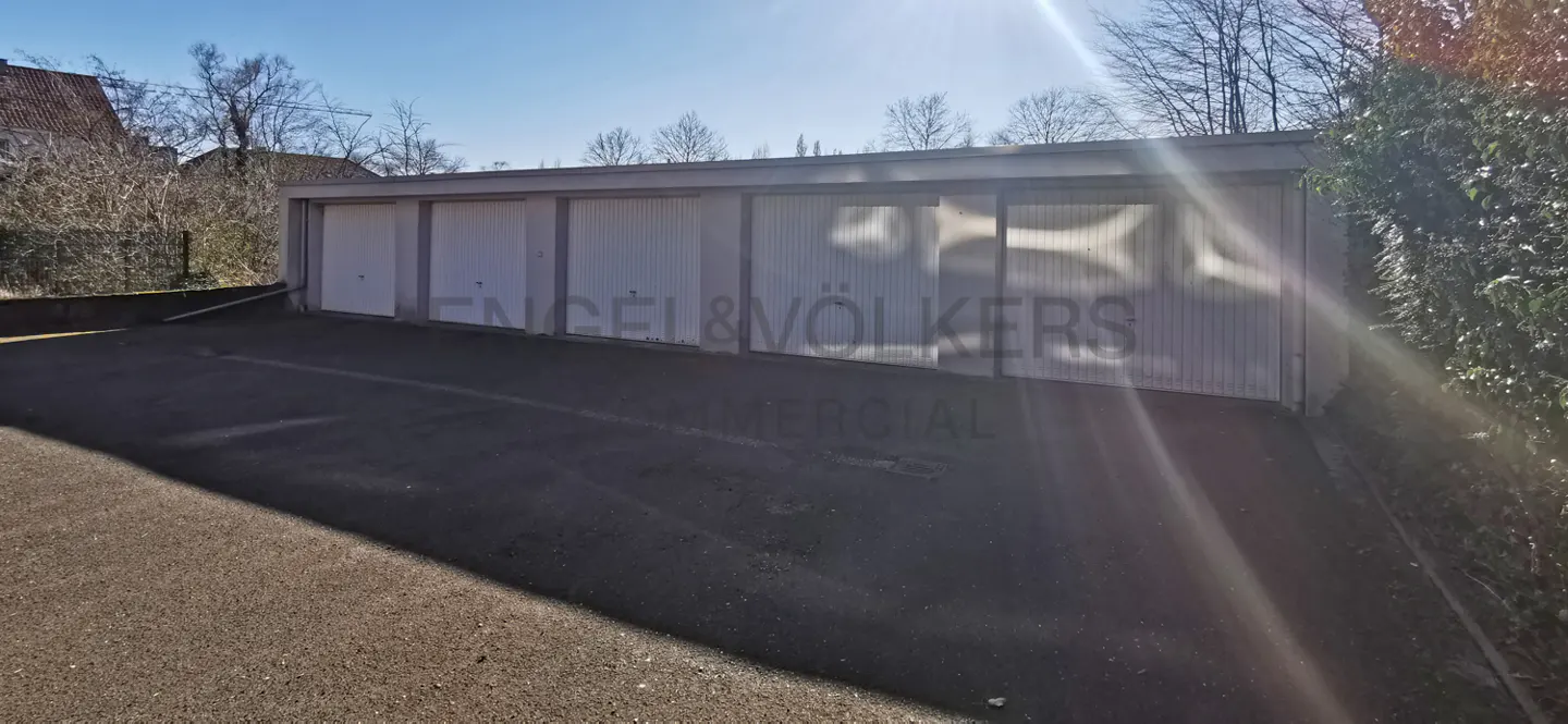 A row of five white garage doors with a paved driveway in front under a bright, sunny sky.