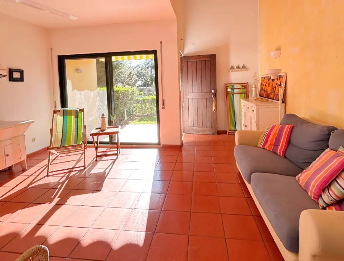 Bright living room with terracotta tile floor, blue sofa with striped pillows, and a sliding glass door to a green yard.
