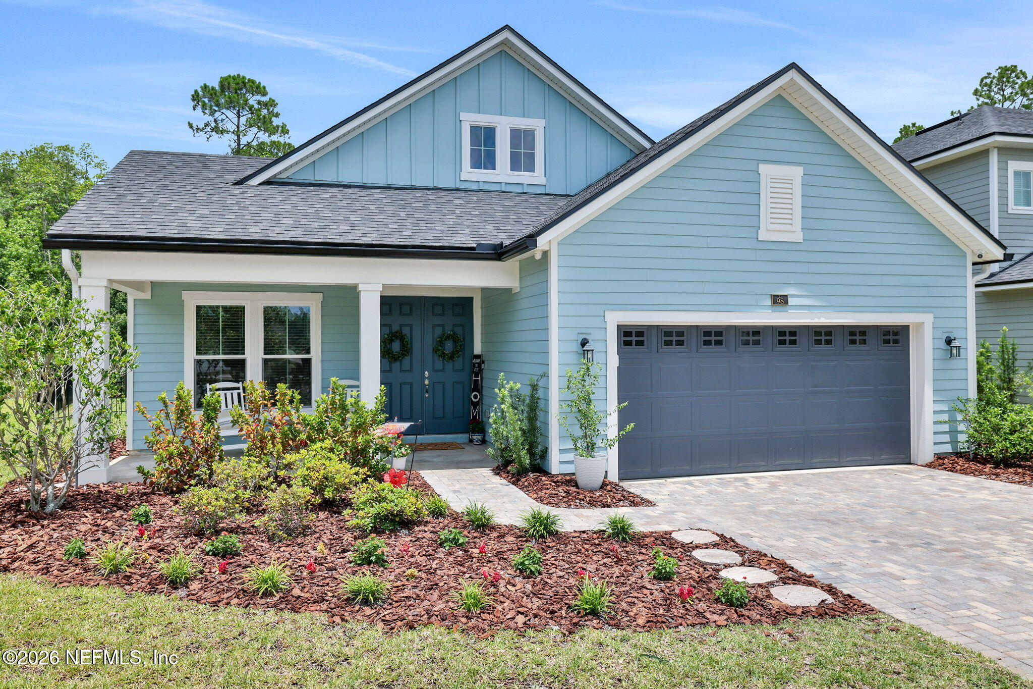 Single-story light blue house with a dark gray garage, double front doors, and a landscaped front yard with mulch.