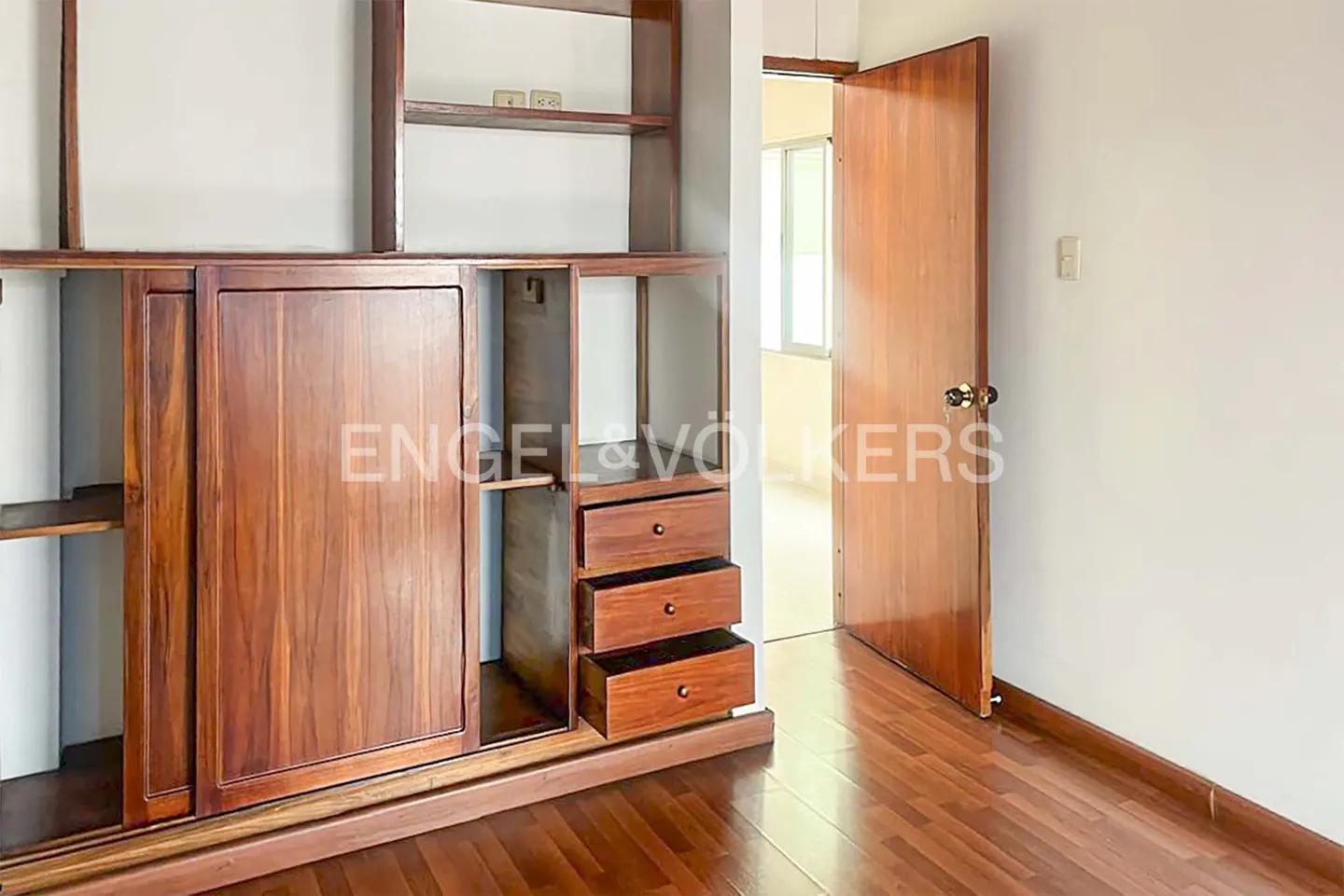 A bedroom with a wooden floor, a built-in wooden wardrobe, and an open wooden door.