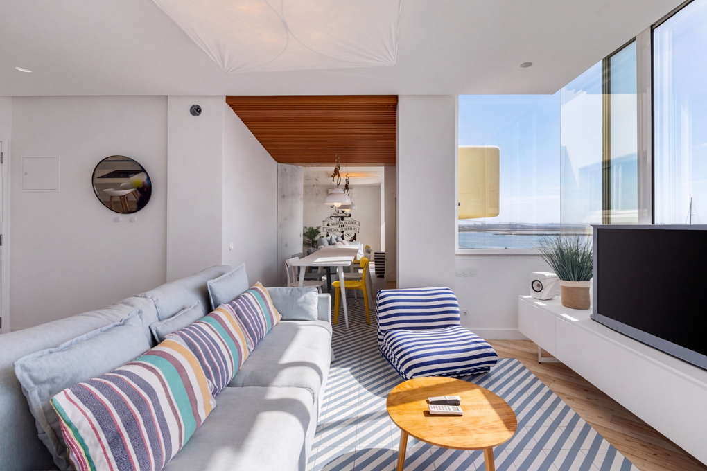 Modern living room with a striped sofa, blue-and-white striped chair, wood coffee table, and large window with water view. [AI-generated text]