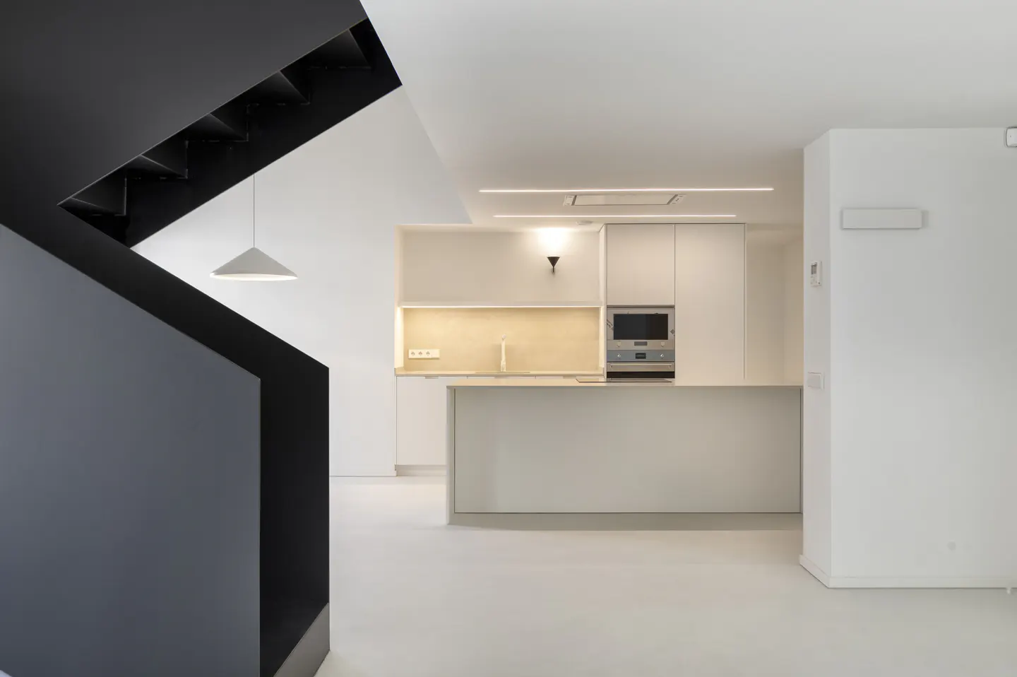 Modern kitchen with white cabinets, island, and stainless steel microwave. Black staircase and pendant light are visible.