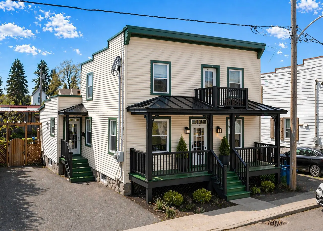 Two-story beige house with green trim and black porch and balcony under a blue sky.