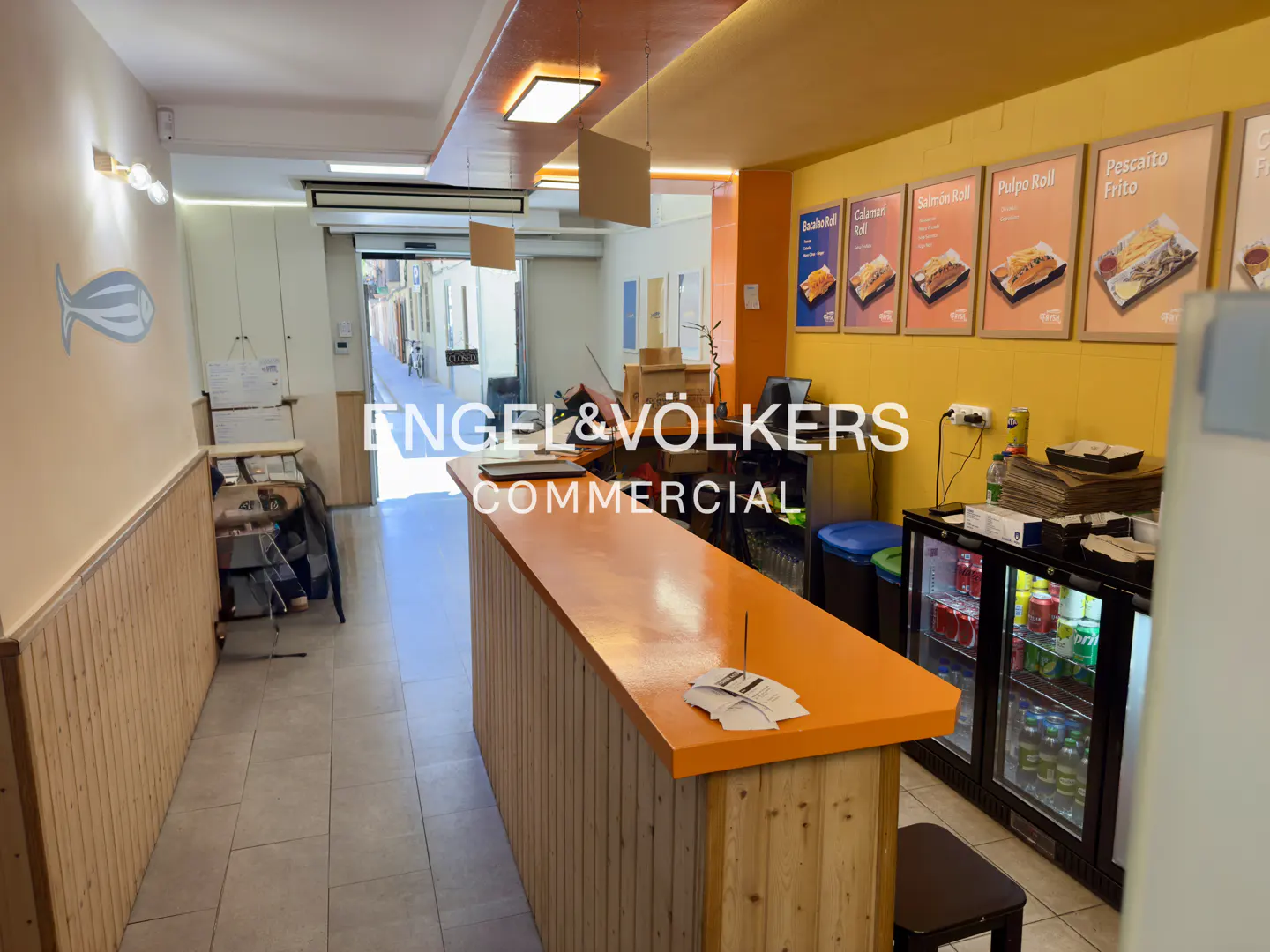Interior view of a commercial space with an orange counter, drink coolers, and menu boards on a yellow wall.
