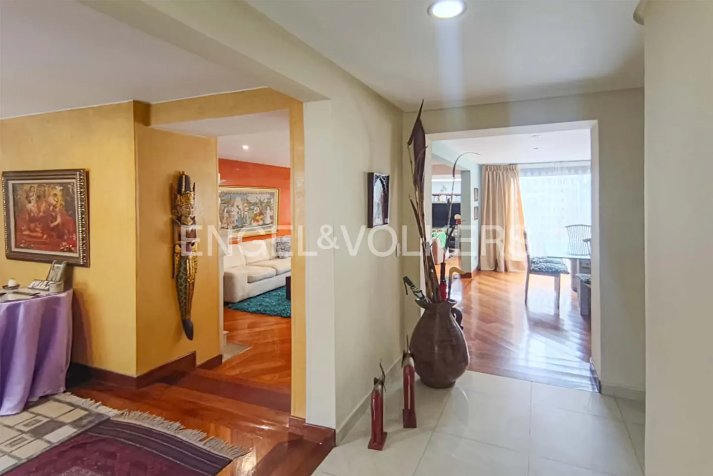 Interior view of a home with a hallway leading to a living room and dining area. The walls are painted in warm tones, and the floors are a mix of wood and tile.