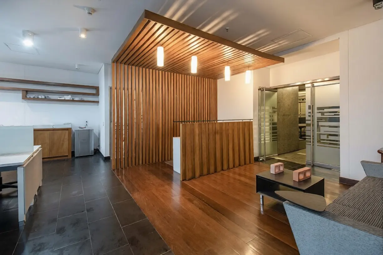 Interior view of an office space with wood floors, a wood slat wall, and a gray sofa. Sliding glass doors are in the background.