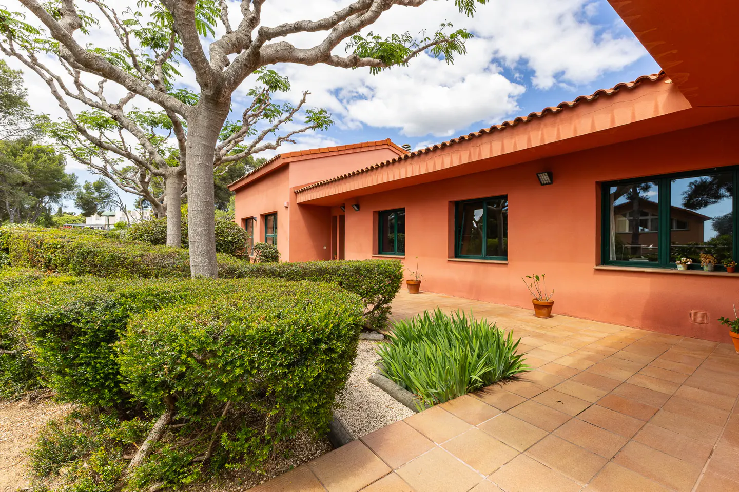 Exterior of an orange single-story house with green window frames, tile roof, and manicured green hedges.