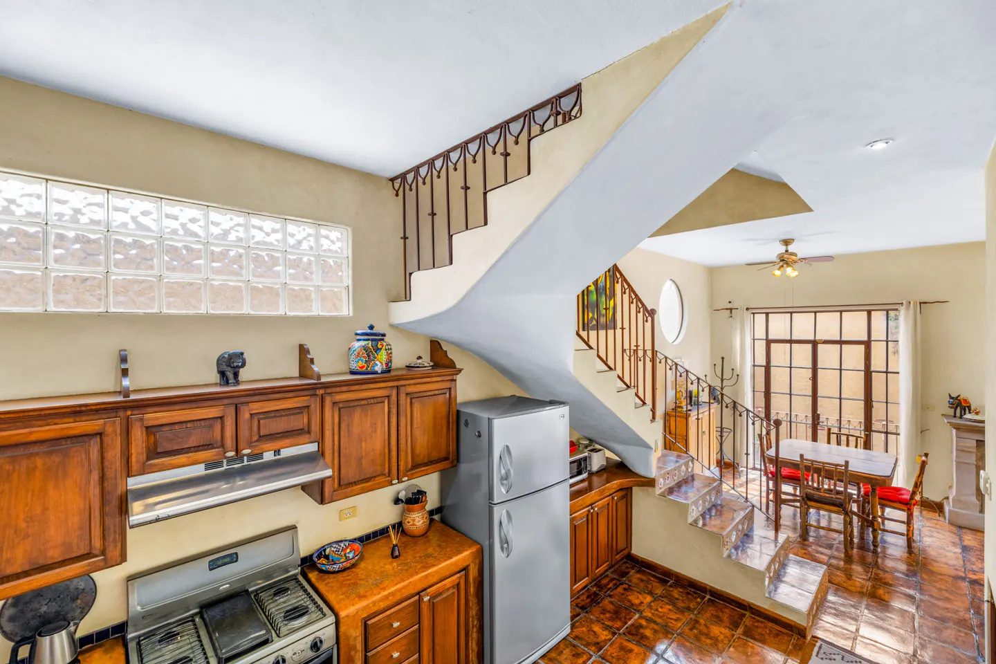 A kitchen with wood cabinets, stainless steel appliances, and a staircase leading to a dining area with a table and chairs.