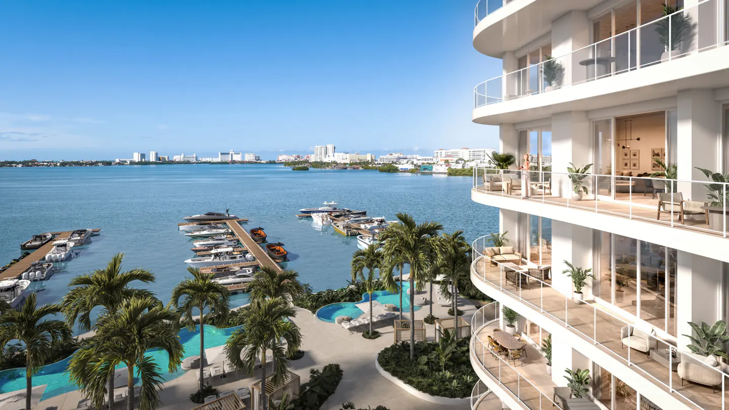 Luxury white condo building overlooking a marina with yachts, palm trees, and a blue ocean under a clear sky.