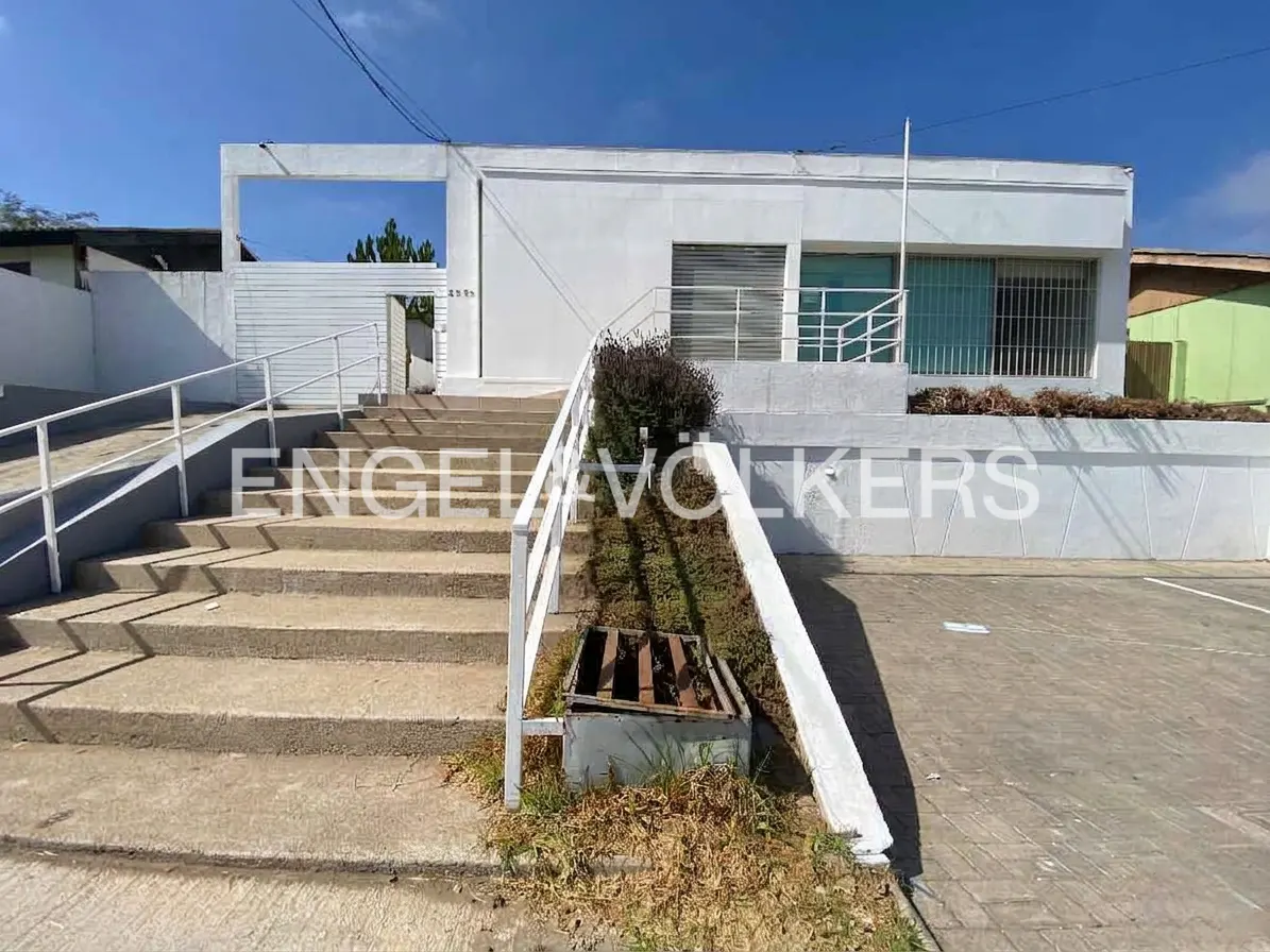 Exterior of a white, modern building with stairs and a ramp leading to the entrance. The sky is blue.