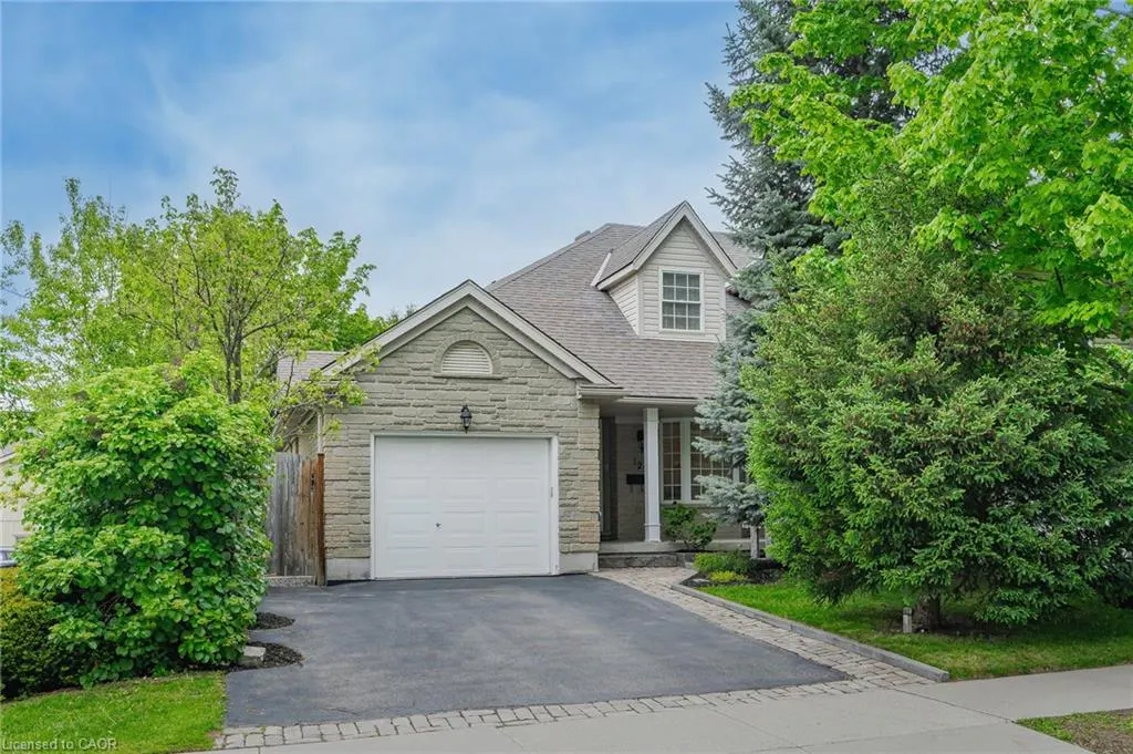 A one-story stone house with a white garage door and green trees.