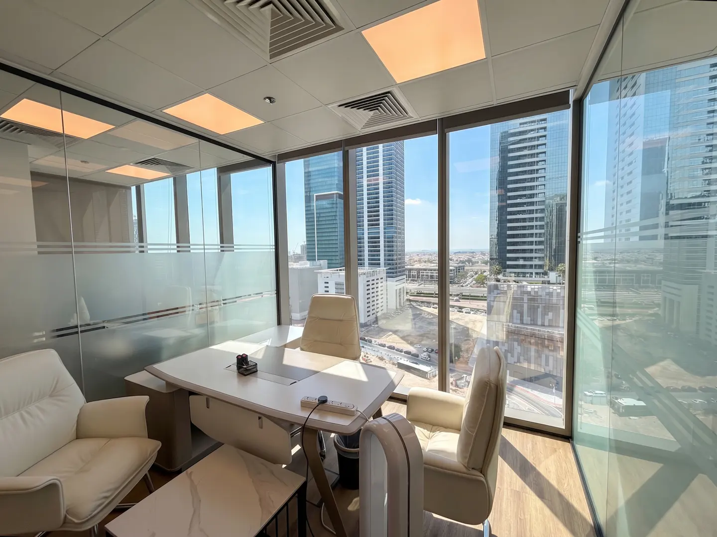 Bright office space with a white desk, chairs, and a large window view of city buildings.