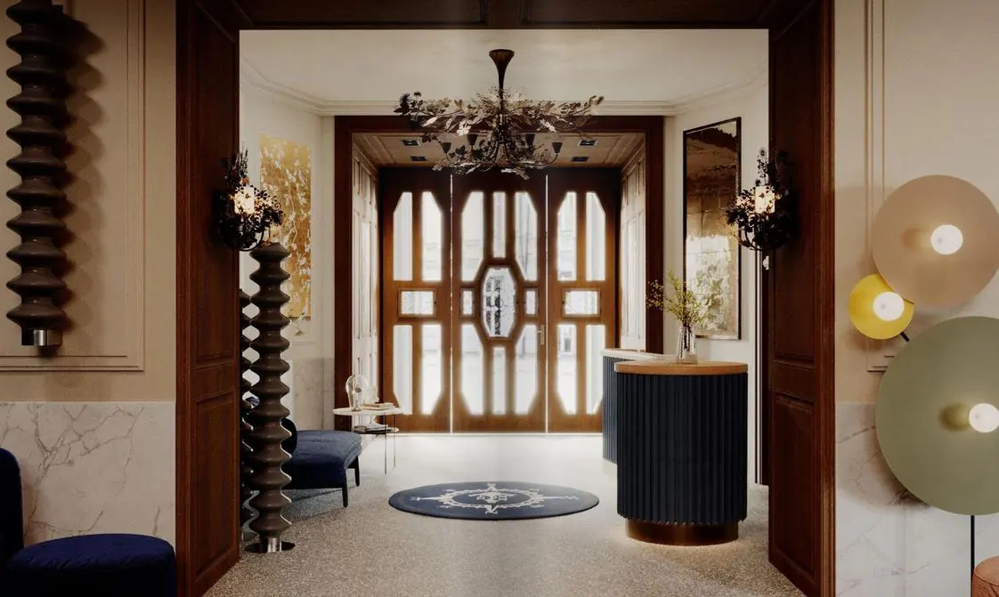 Elegant entryway with dark wood doors, a decorative chandelier, and unique wall sconces. A round rug sits on the speckled floor.