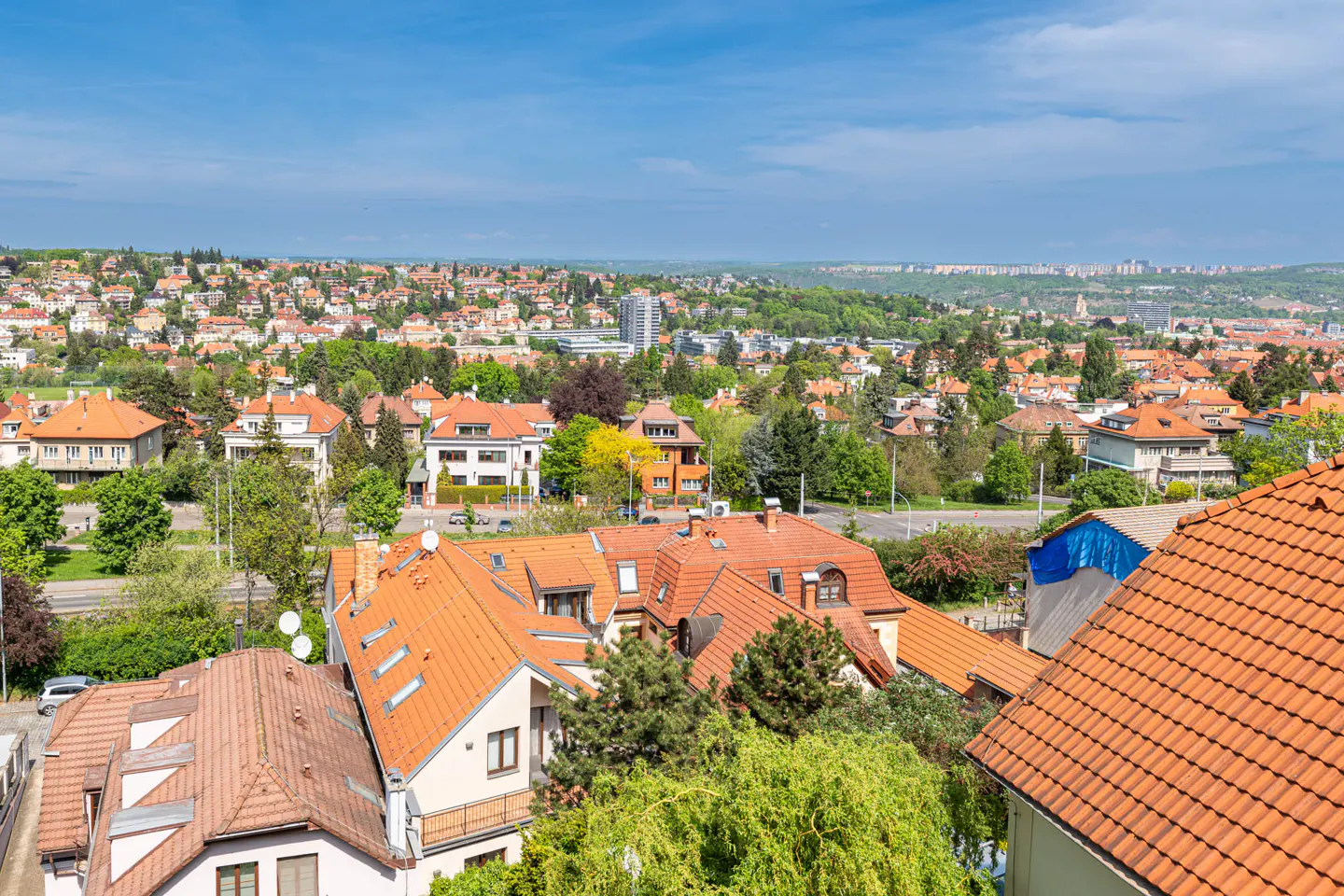 A high-angle view of a neighborhood with houses with orange roofs and green trees under a blue sky.