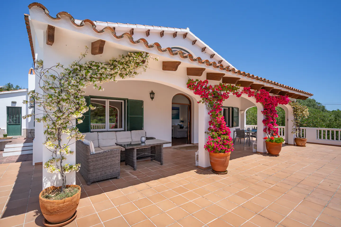 Exterior view of a white villa with a terracotta tile roof and patio, adorned with flowering vines.