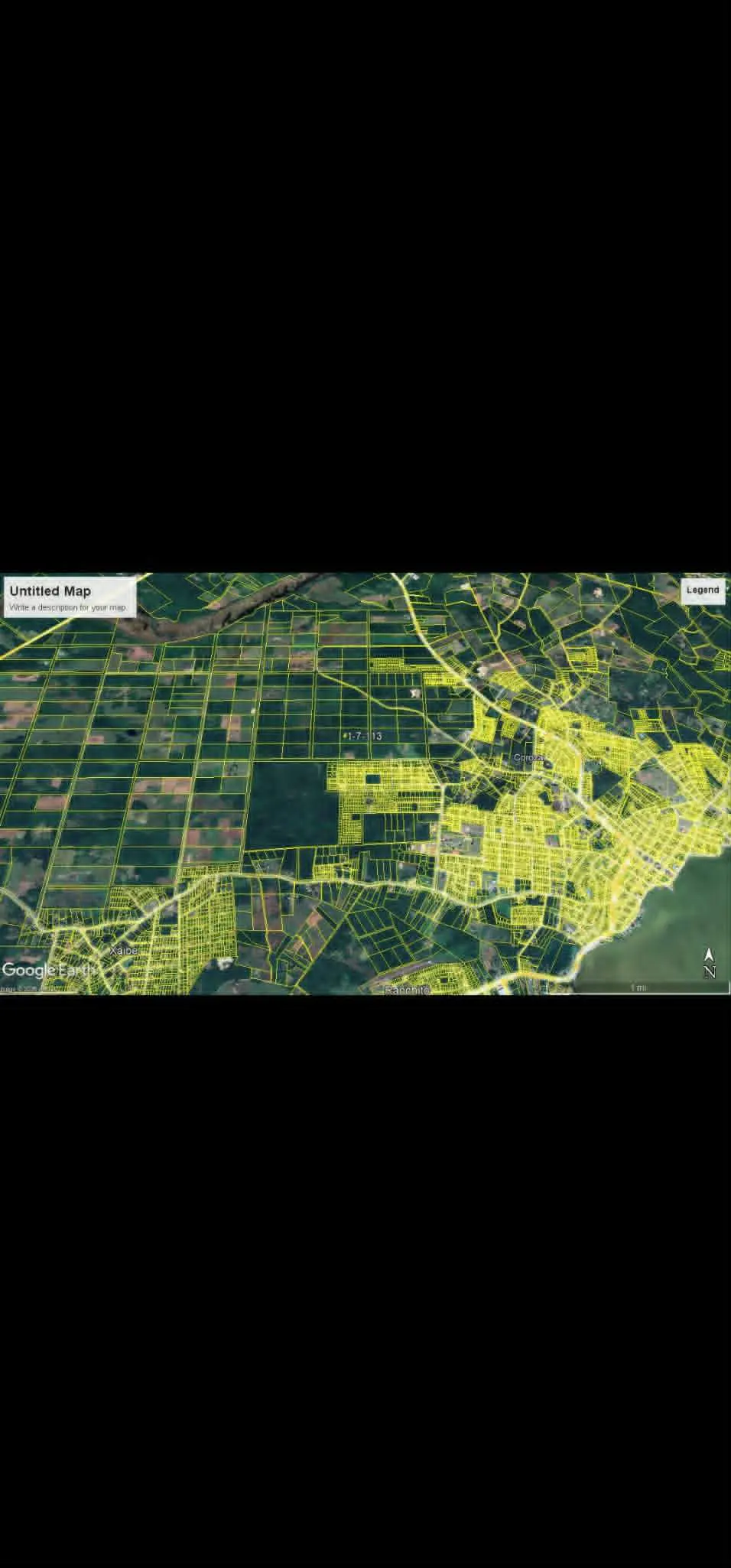 Aerial view of a city and farmland, divided into plots with yellow lines, next to a body of water.