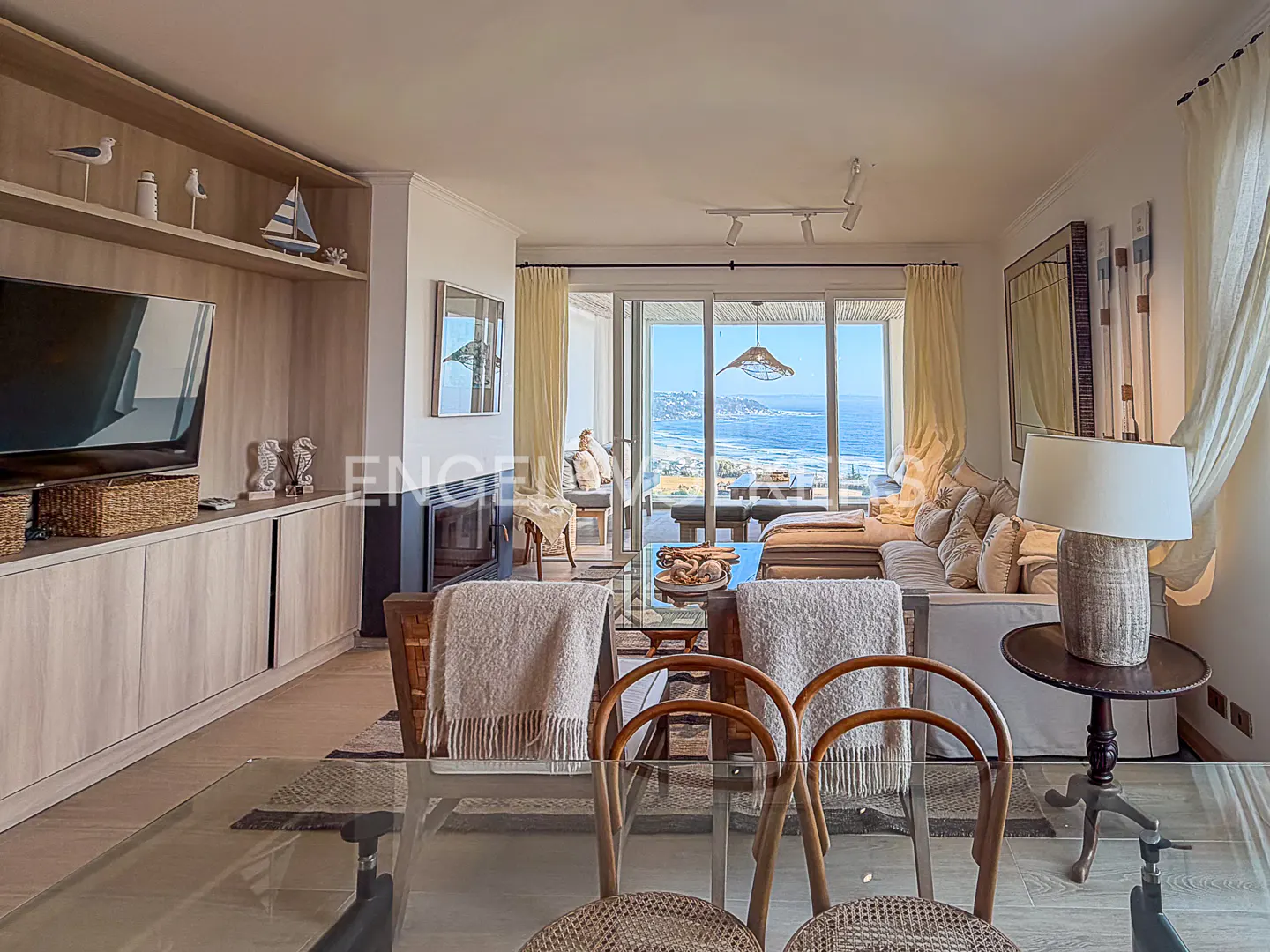 Living room with ocean view. Glass table and chairs in foreground, sofa and balcony overlooking the ocean in background.