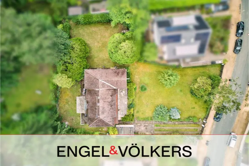 Aerial view of a house with a brown roof, surrounded by green grass and trees. Engel & Völkers logo at the bottom.
