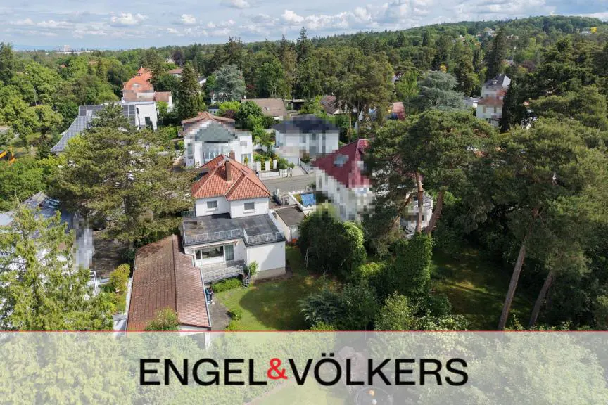 Aerial view of a white house with a red tiled roof surrounded by lush green trees and a residential neighborhood.
