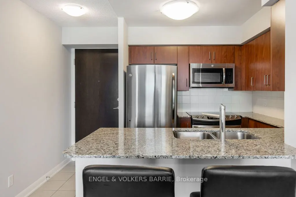 A kitchen with stainless steel appliances, wood cabinets, and a granite countertop island with black leather stools.
