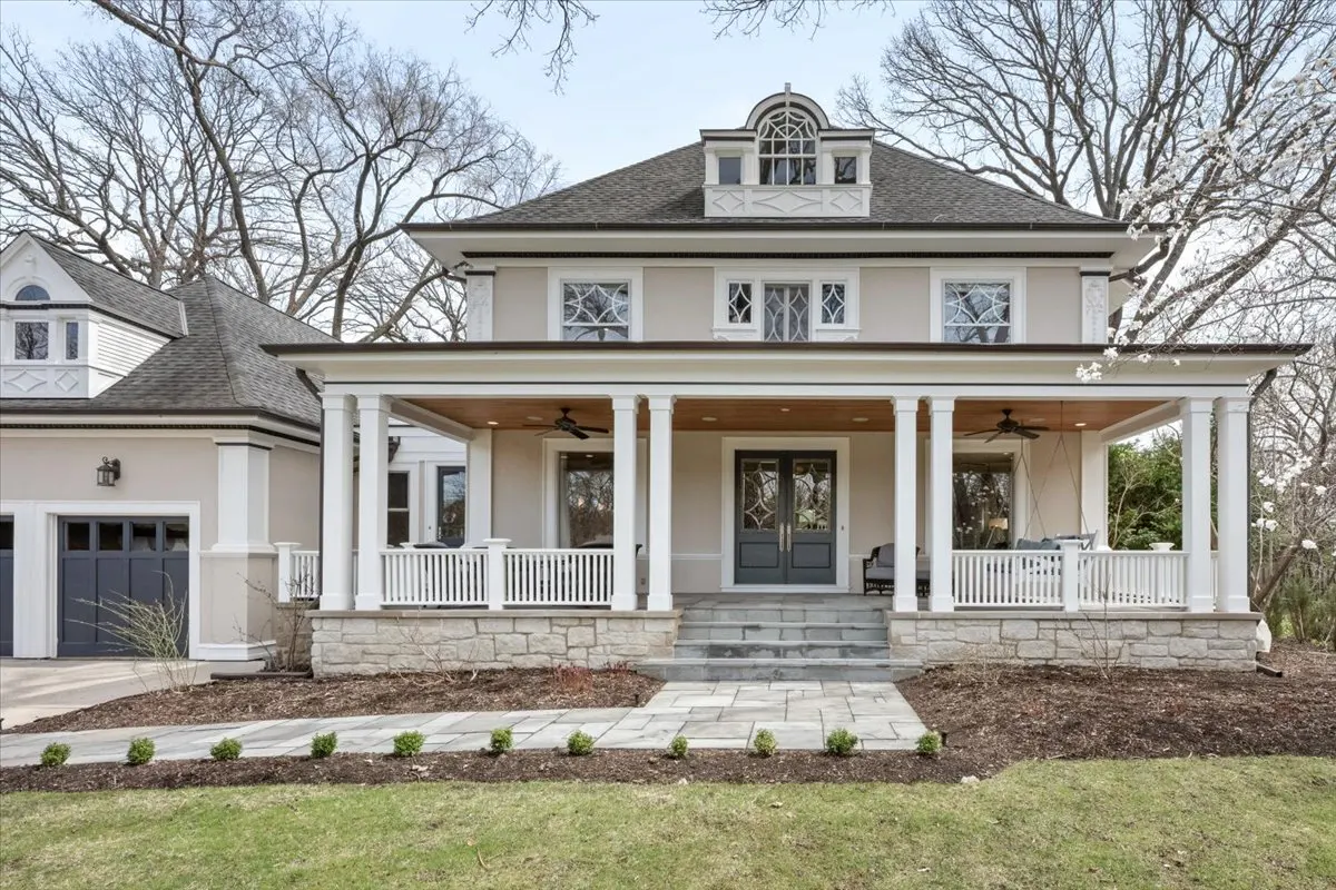 Beige two-story house with a gray roof, white pillars, and a large front porch. A stone walkway leads to the front door.