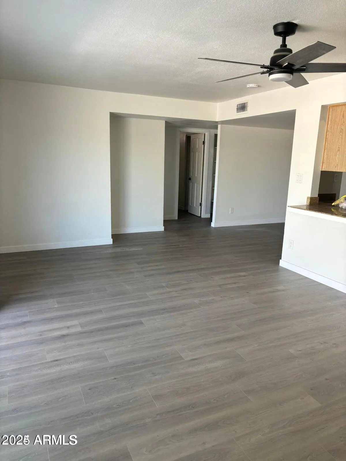 An empty living room with gray wood floors, white walls, and a black ceiling fan.