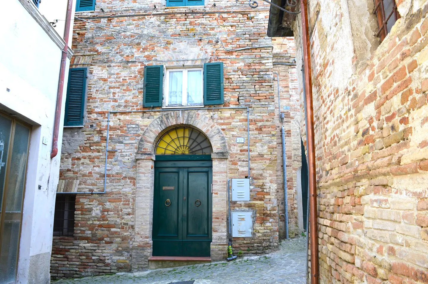 A brick building with a green door and window shutters on a narrow street.