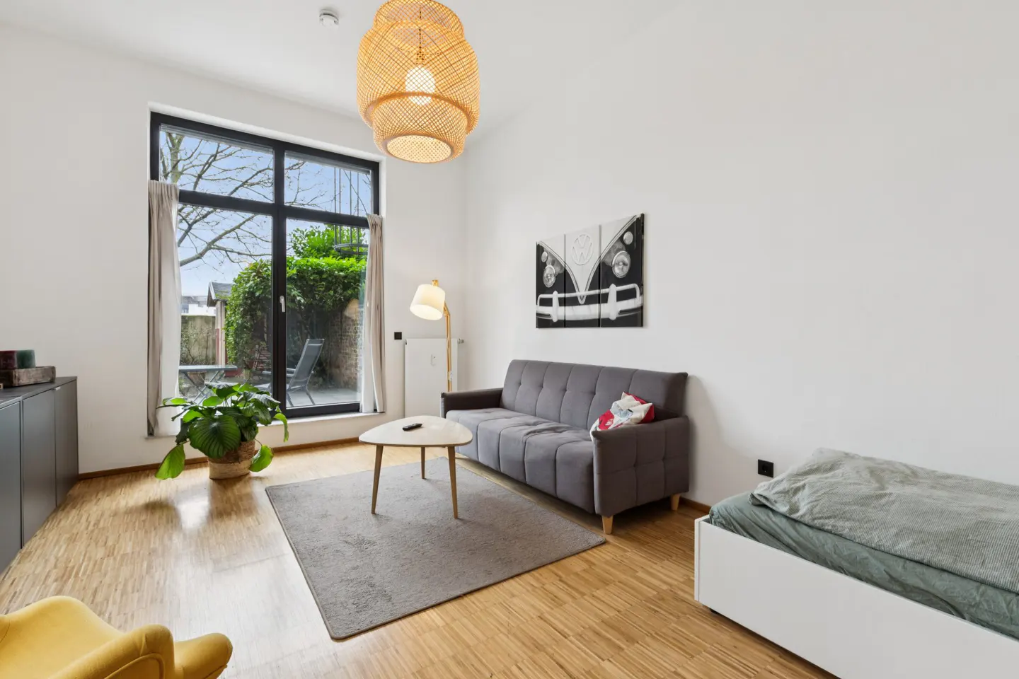 Bright living room with wood floors, a gray sofa, a white coffee table, and a large window overlooking a green garden.