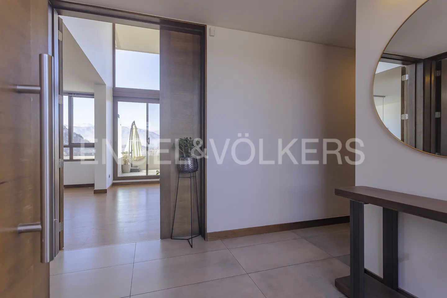 Entryway view with open wood door, tile floor, console table, round mirror, and balcony with mountain view.