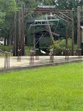 Construction site with wooden beams and metal supports on a concrete foundation, green grass in the foreground.