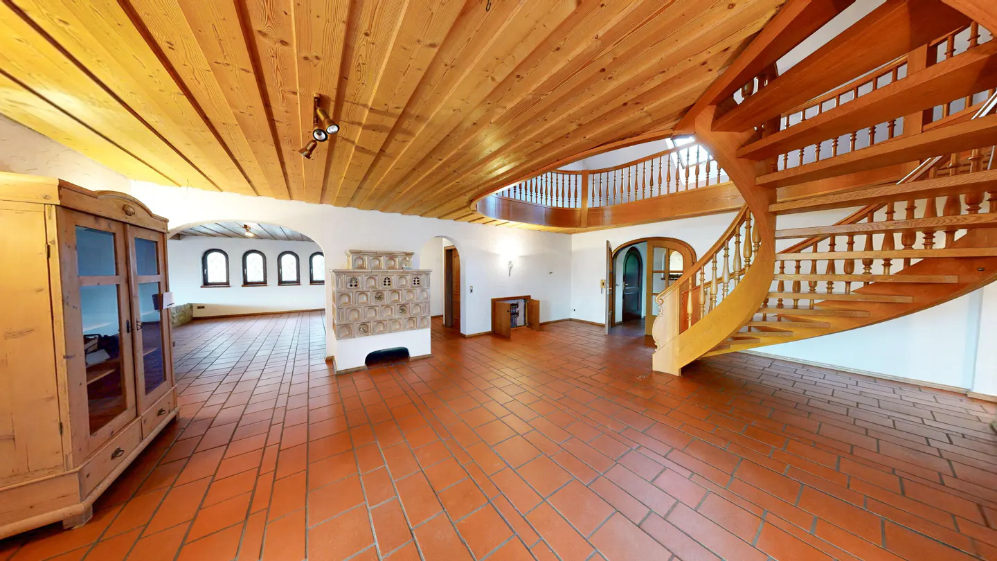 A spacious room with a wooden ceiling, terracotta tile floor, and a winding wooden staircase.