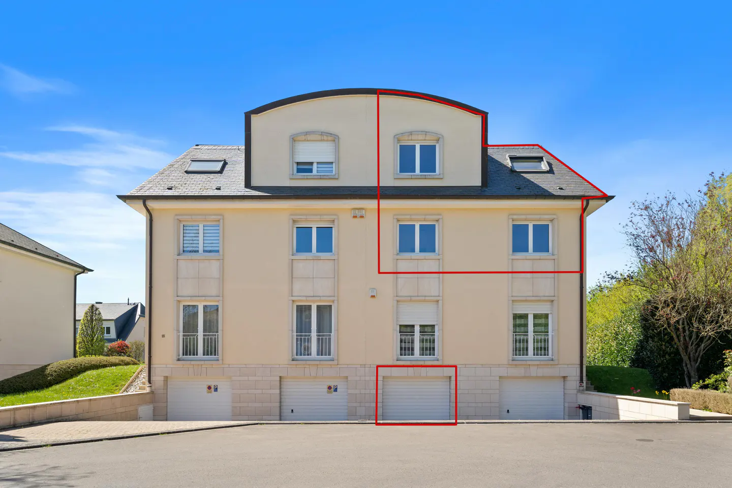 Three-story beige apartment building with white garage doors on the ground floor under a clear blue sky.