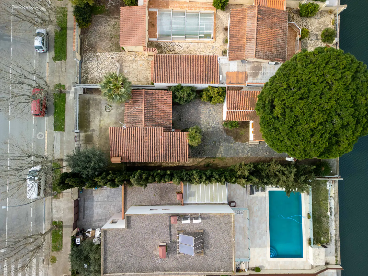 Aerial view of houses with red tile roofs, a pool, and a street with cars and trees.