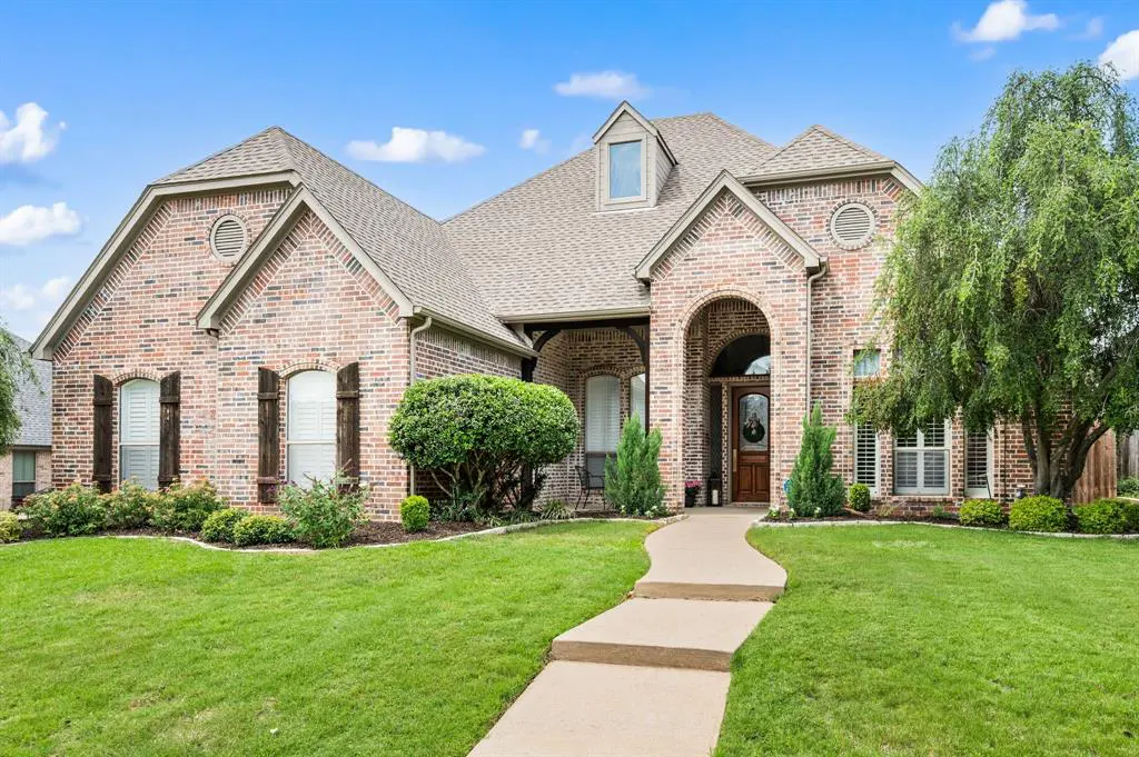 A single-story brick house with a brown roof, arched entryway, and green lawn under a blue sky.