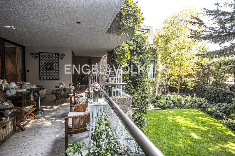 A balcony with wicker furniture overlooks a green lawn and trees. The building is covered in ivy. An Engel & Volkers logo is visible.