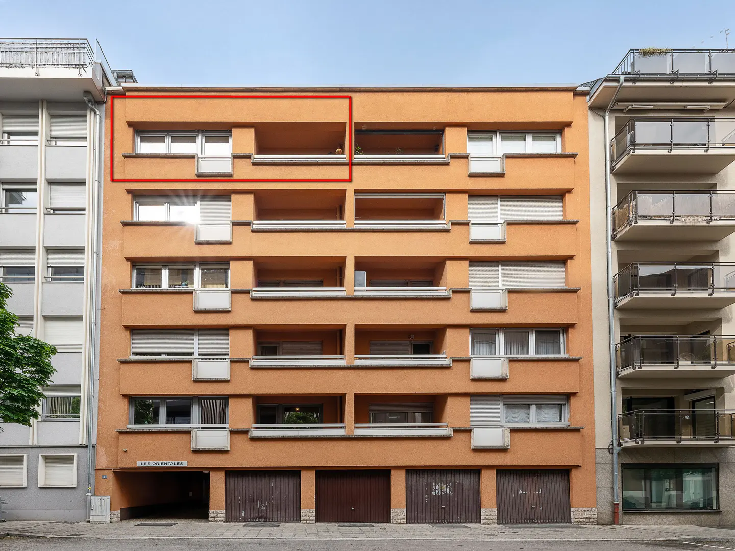 Exterior of a six-story orange apartment building with balconies and garage doors on the ground floor.