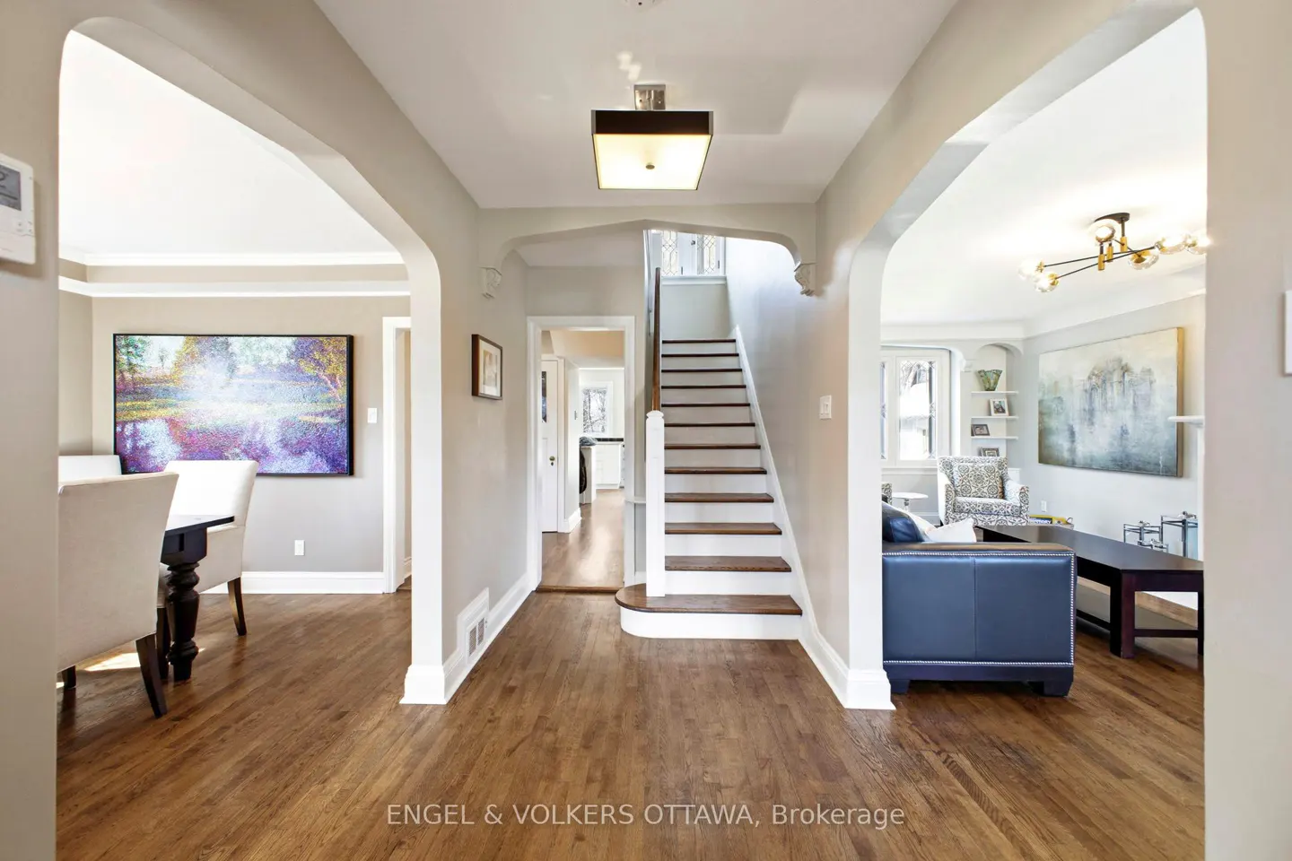 A bright foyer with hardwood floors, arched doorways, and a staircase. A dining room and living room are visible.