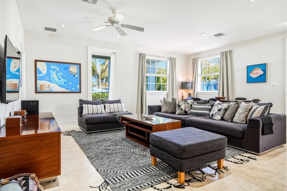 Living room with gray sofas, a wood coffee table, and a black and white patterned rug. Windows offer views of palm trees and blue water.